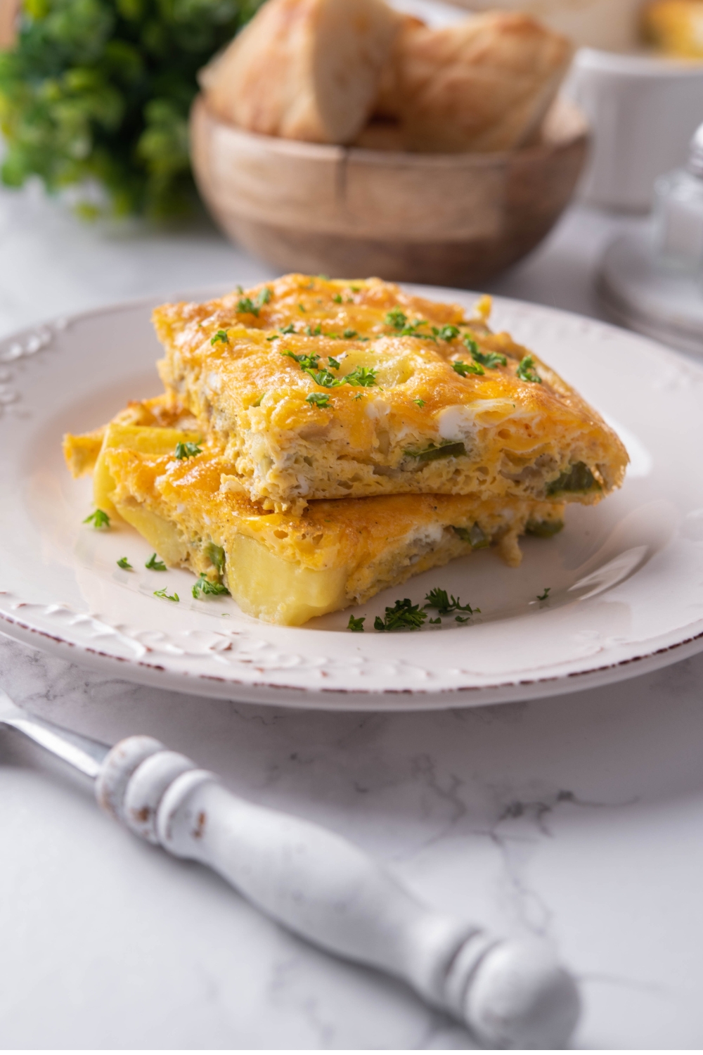 A plate with two slices of breakfast potato casserole garnished with fresh herbs.