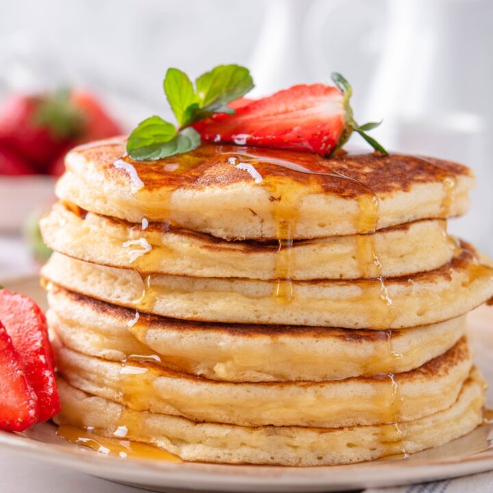 A stack of six Bisquick pancakes with maple syrup dripping down the sides