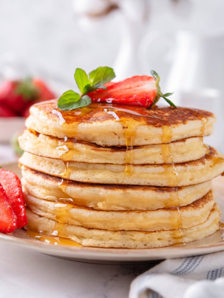 A stack of six Bisquick pancakes with maple syrup dripping down the sides