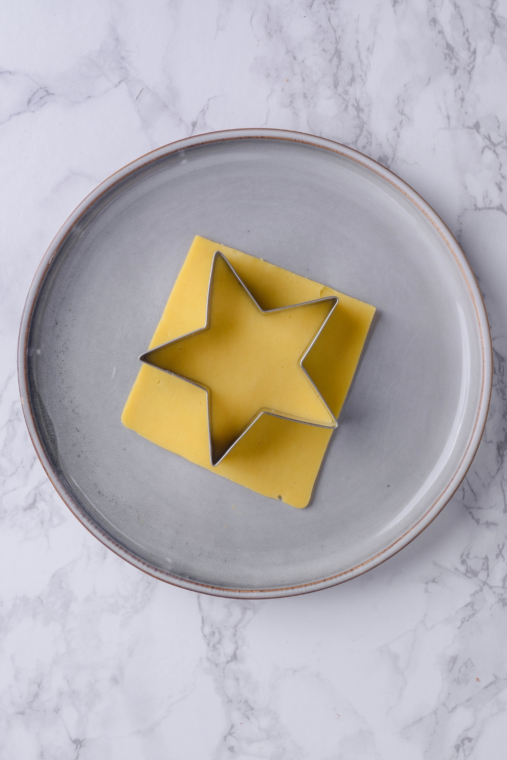 A plate with a slice of cheese being cut out with a star shaped cutter.