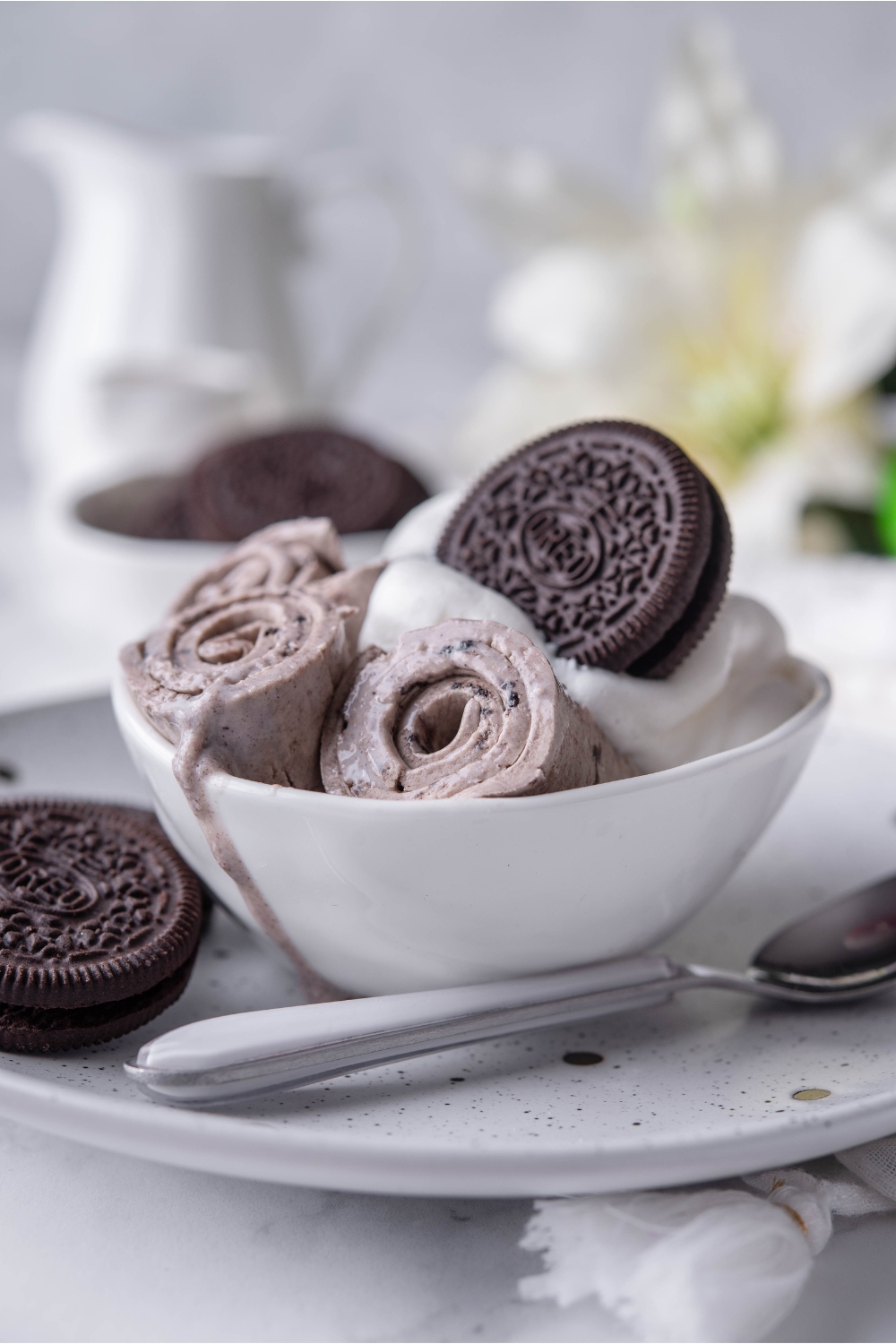 A few ice cream rolls in a bowl with whipped cream and an Oreo.