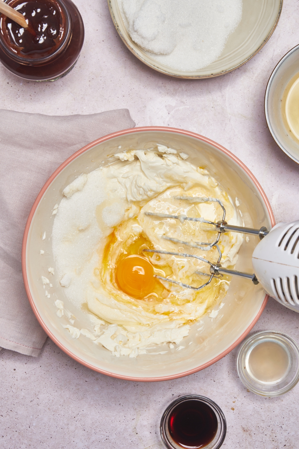 A mixing bowl with the cream cheese mixture, an egg has just been added to it and the electric beater is mixing.
