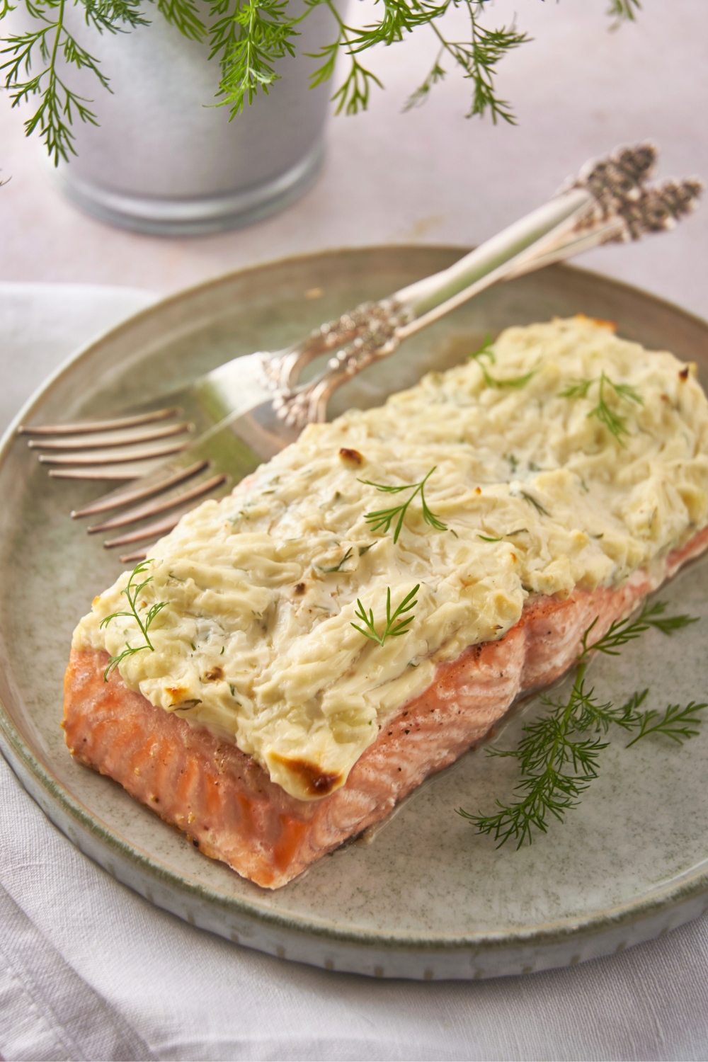 Baked cream cheese and dill on a fillet of salmon on a plate with two forks on it.