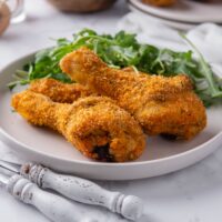 A plate with a green salad and three shake and bake chicken legs.