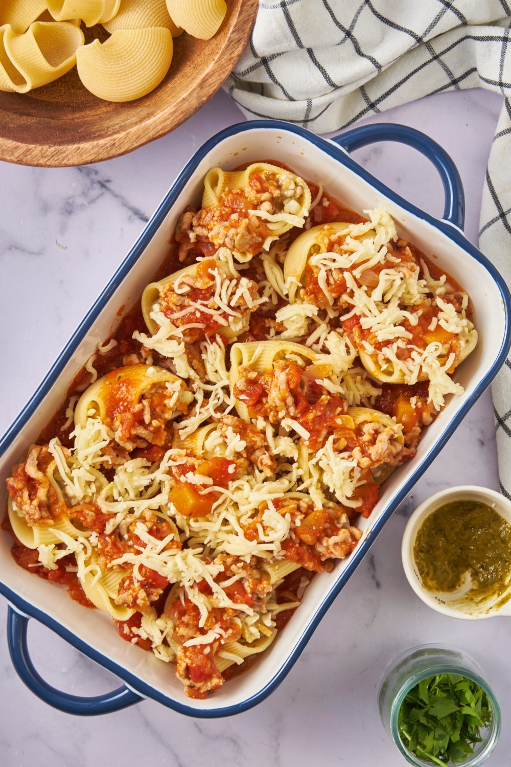 A blue-handled baking dish layered with red sauce, jumbo pasta shells stuffed with meat and cheese, and a layer of shredded cheese covering the pasta.