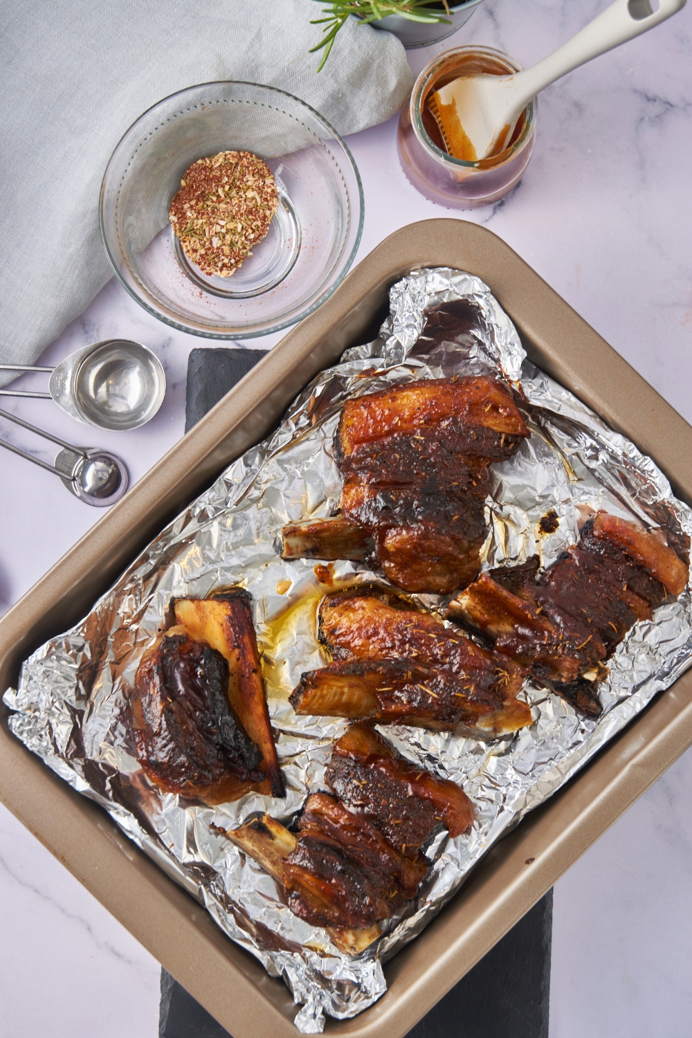 A baking dish lined with foil and filled with baked beef back ribs coated in BBQ sauce.