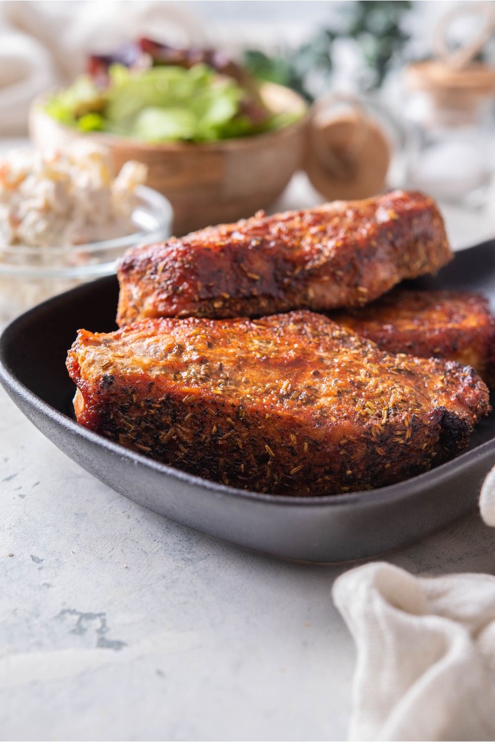 A stack of three seasoned barbecue pork ribs on a black plate.