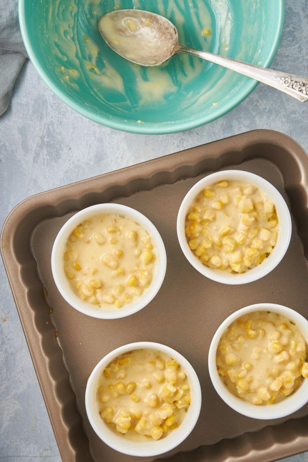 Four ramekins placed in a baking dish and evenly filled with unbaked corn pudding casserole.