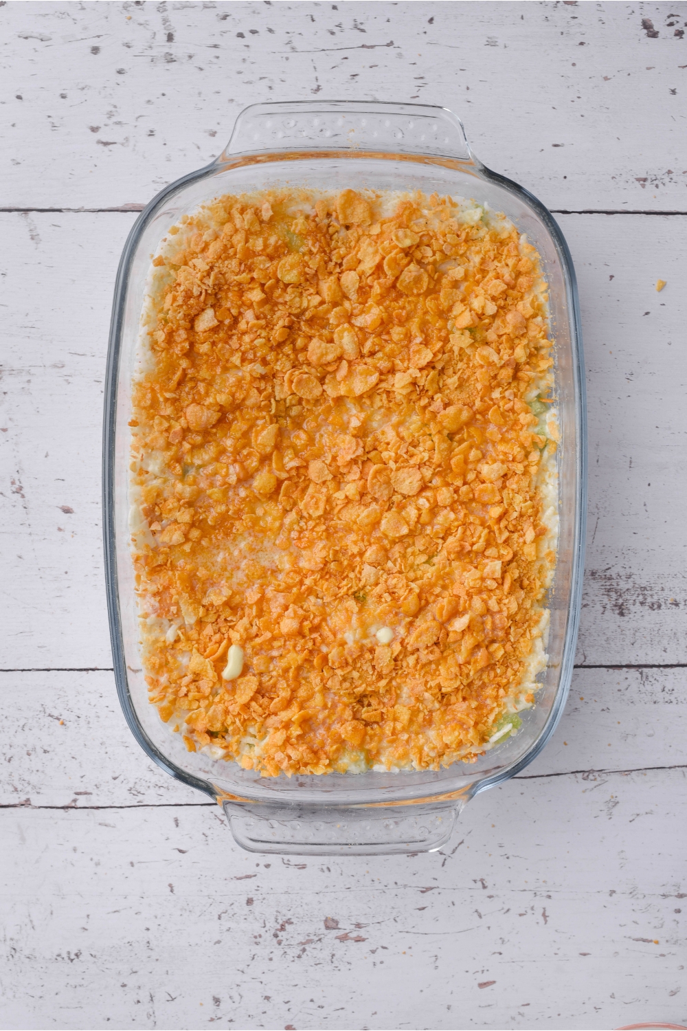 Overhead view of a clear casserole dish filled with unbaked rotisserie chicken casserole that's topped with crushed cornflakes.