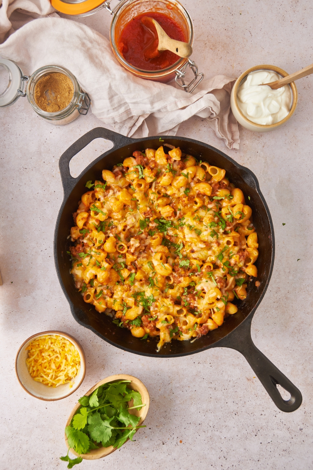 A black cast iron skillet filled with freshly baked taco pasta casserole covered in melted cheese and fresh green herbs.