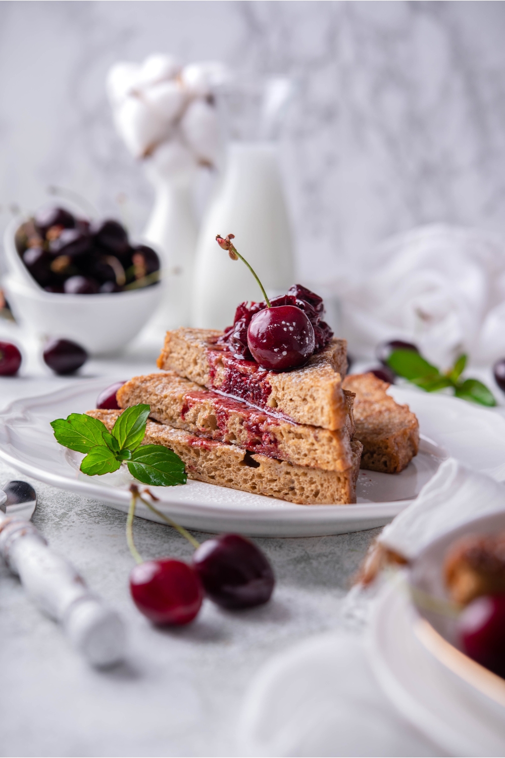 A stack of three pieces of French toast topped with cherry compote, a single cherry, and a mint sprig.