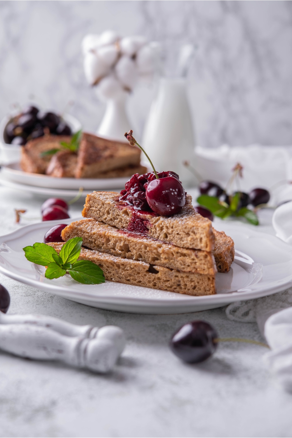 A stack of three pieces of French toast topped with cherry compote, a single cherry, and a mint sprig.