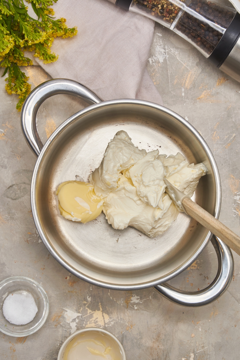 A large pot with cream cheese and butter added to it using a silicone spatula.
