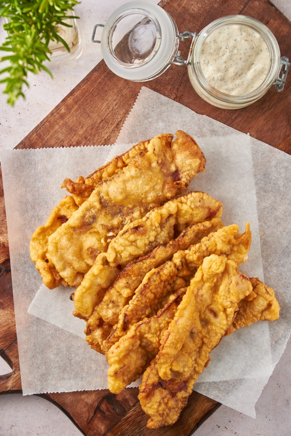A pile of golden brown deep fried bacon spilled out over two sheets of wax paper, next to a jar of dipping sauce.