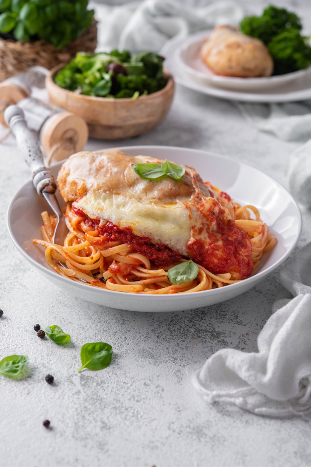 A bowl of chicken parmesan with chicken covered in melted cheese, a garnish of fresh basil, and served on a bed of pasta with marinara sauce.