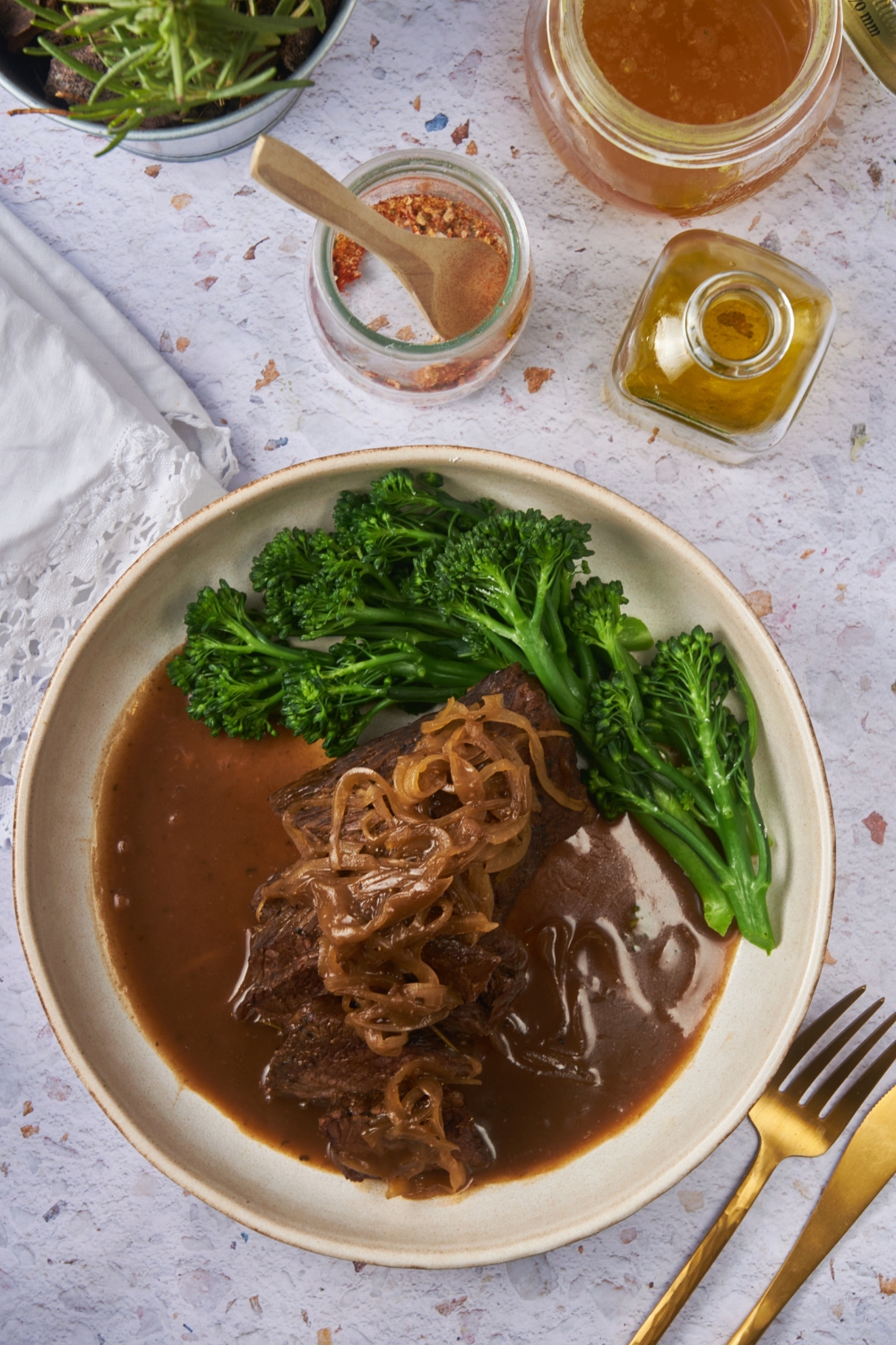 Overhead view of a sirloin roast topped with caramelized onions and covered in a brown gravy, with a side of broccoli.
