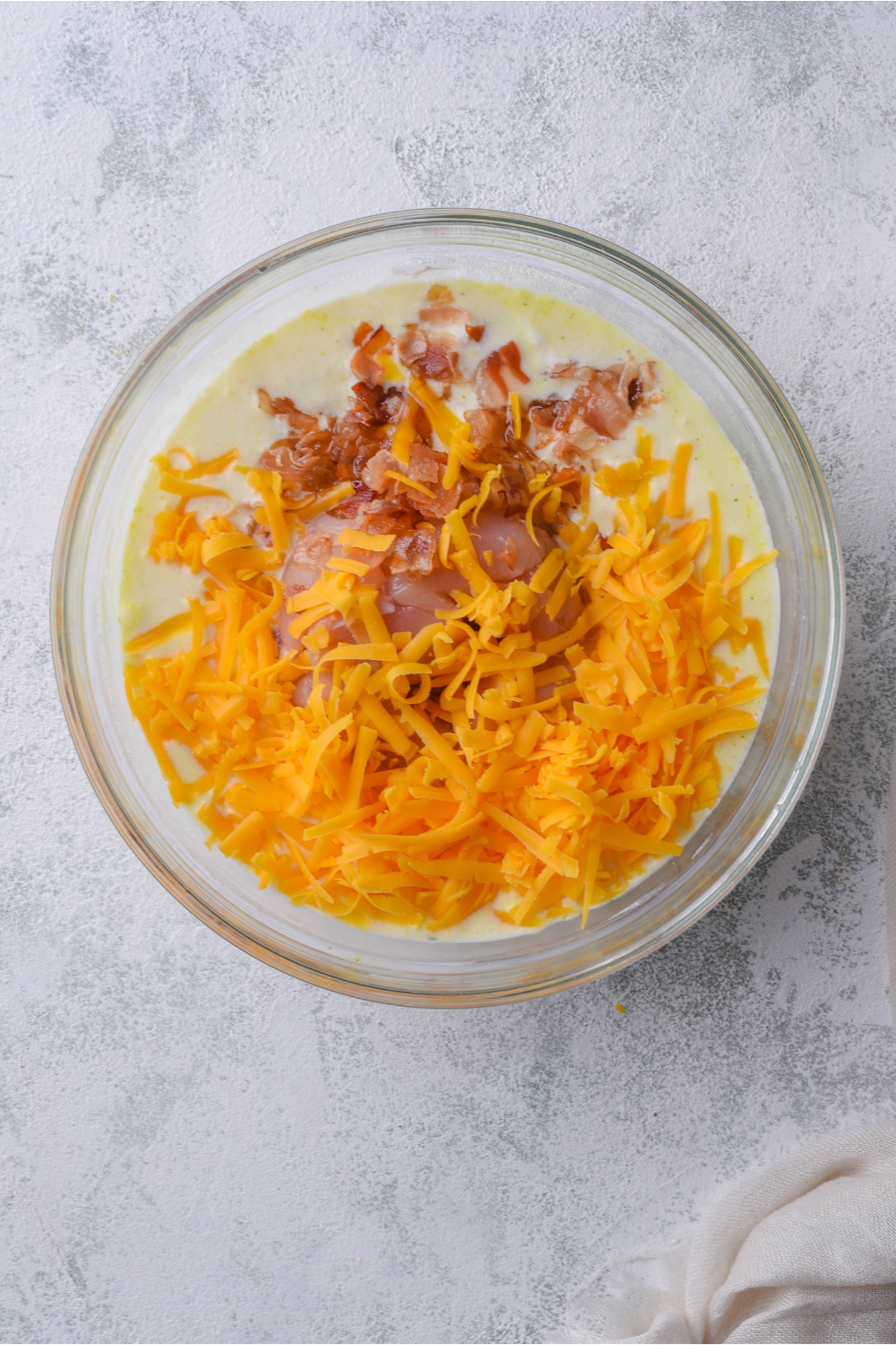 A clear bowl filled with chopped bacon and shredded cheddar cheese in a yellow cream sauce.