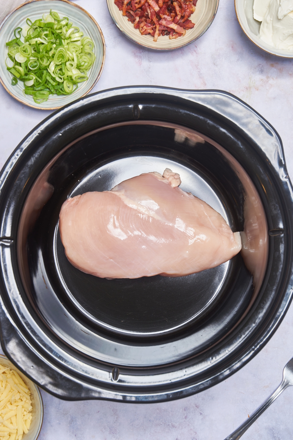A raw chicken breast in the bottom of a slow cooker.
