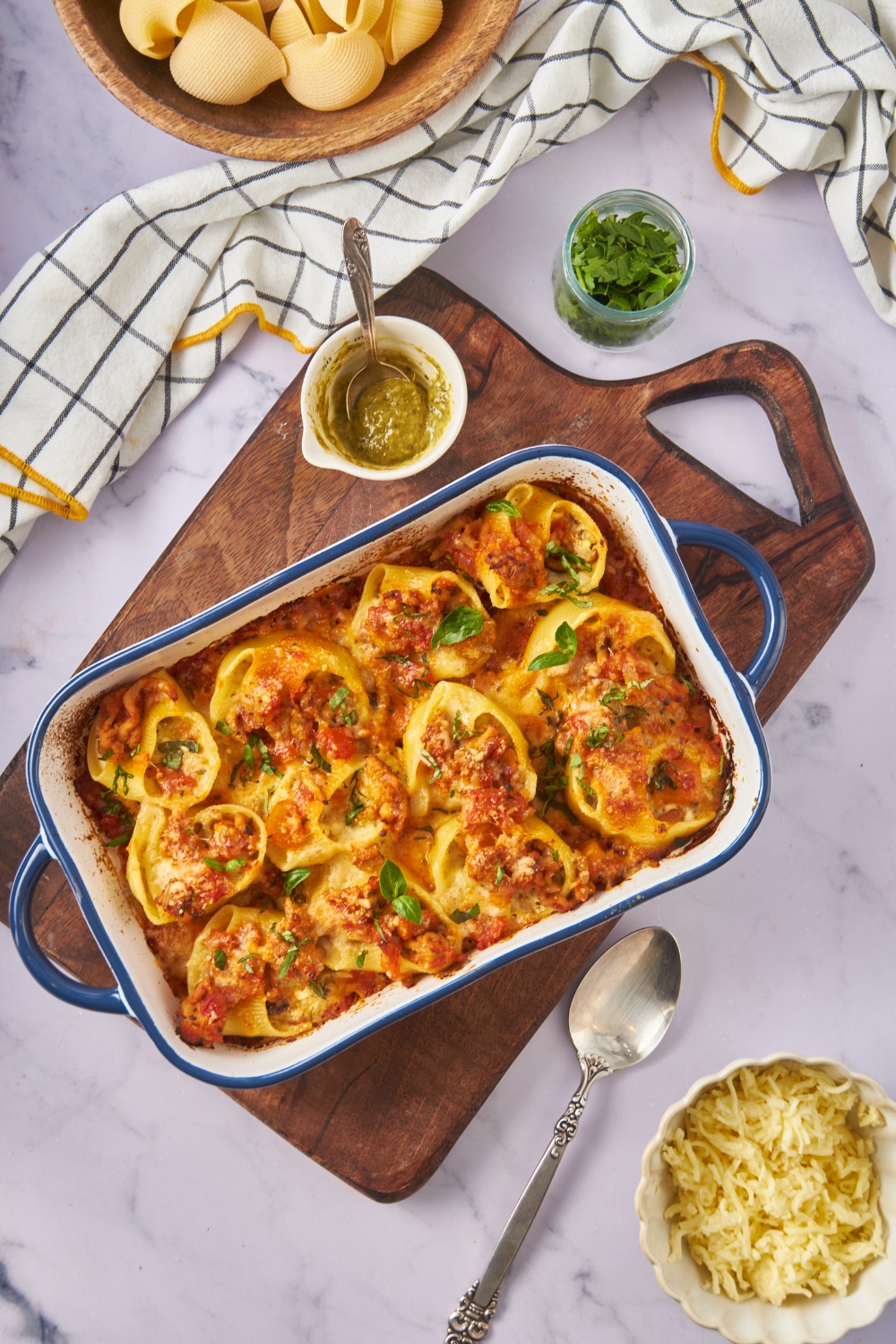 Overhead view of a baking dish filled with freshly baked pasta shells stuffed with meat and covered with melted cheese and fresh herbs.