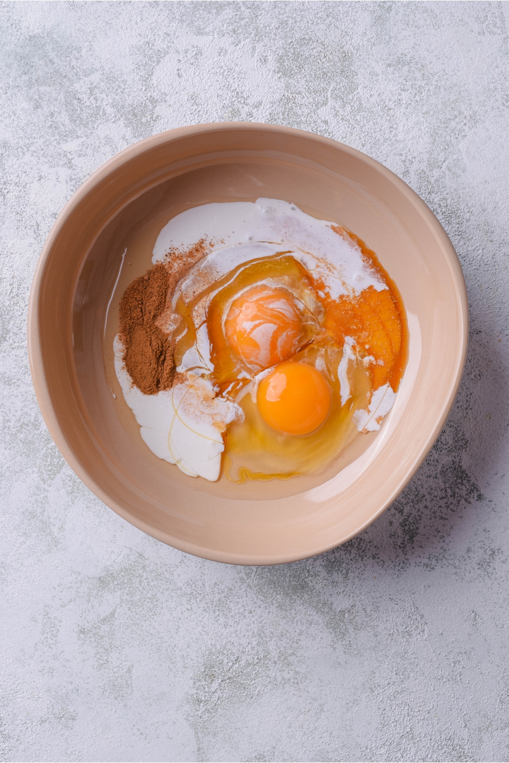 A bowl filled with two unbeaten eggs, cream, cinnamon, and vanilla extract.
