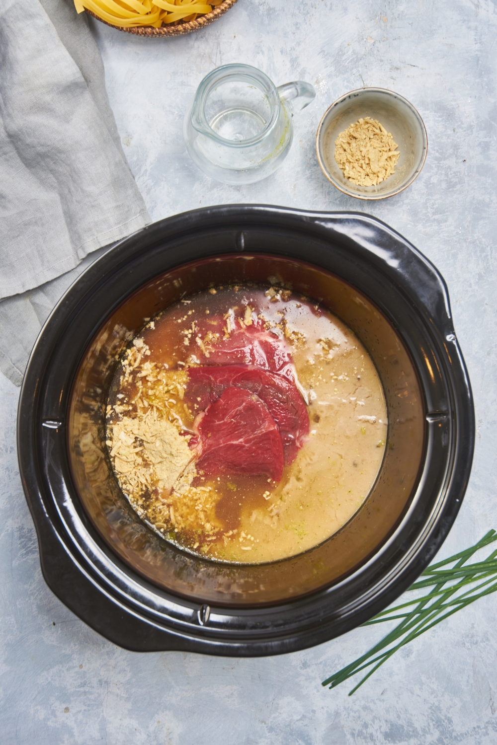 Black crockpot with raw cube steak, dry soup mix, a creamy soup mixture, and broth.