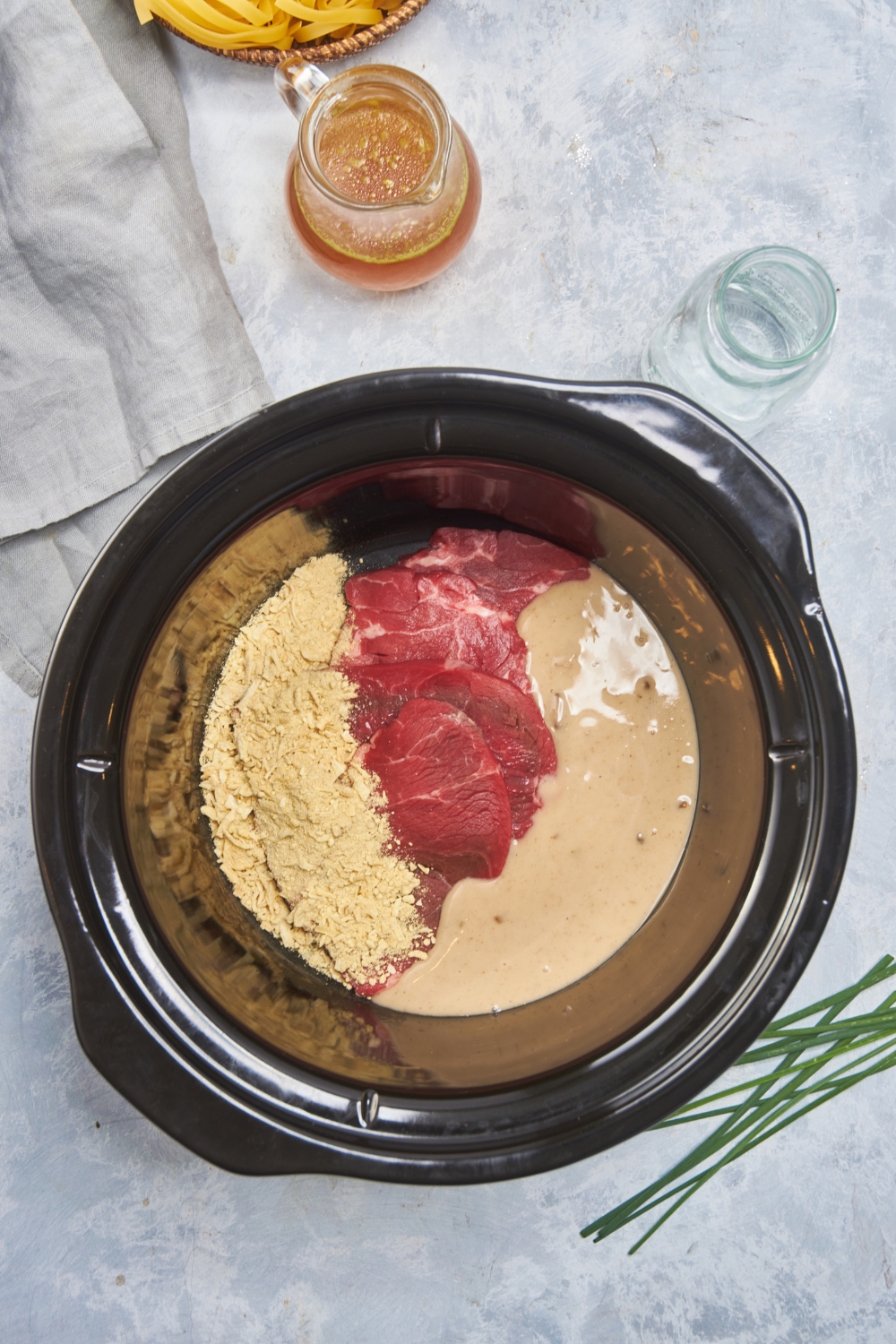 Black crockpot filled with raw cube steak, creamy soup, and a dry soup mix. The ingredients have not been mixed together.