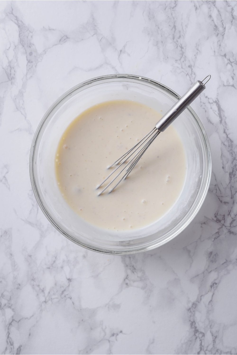 A clear bowl with creamy soup and a whisk in it.