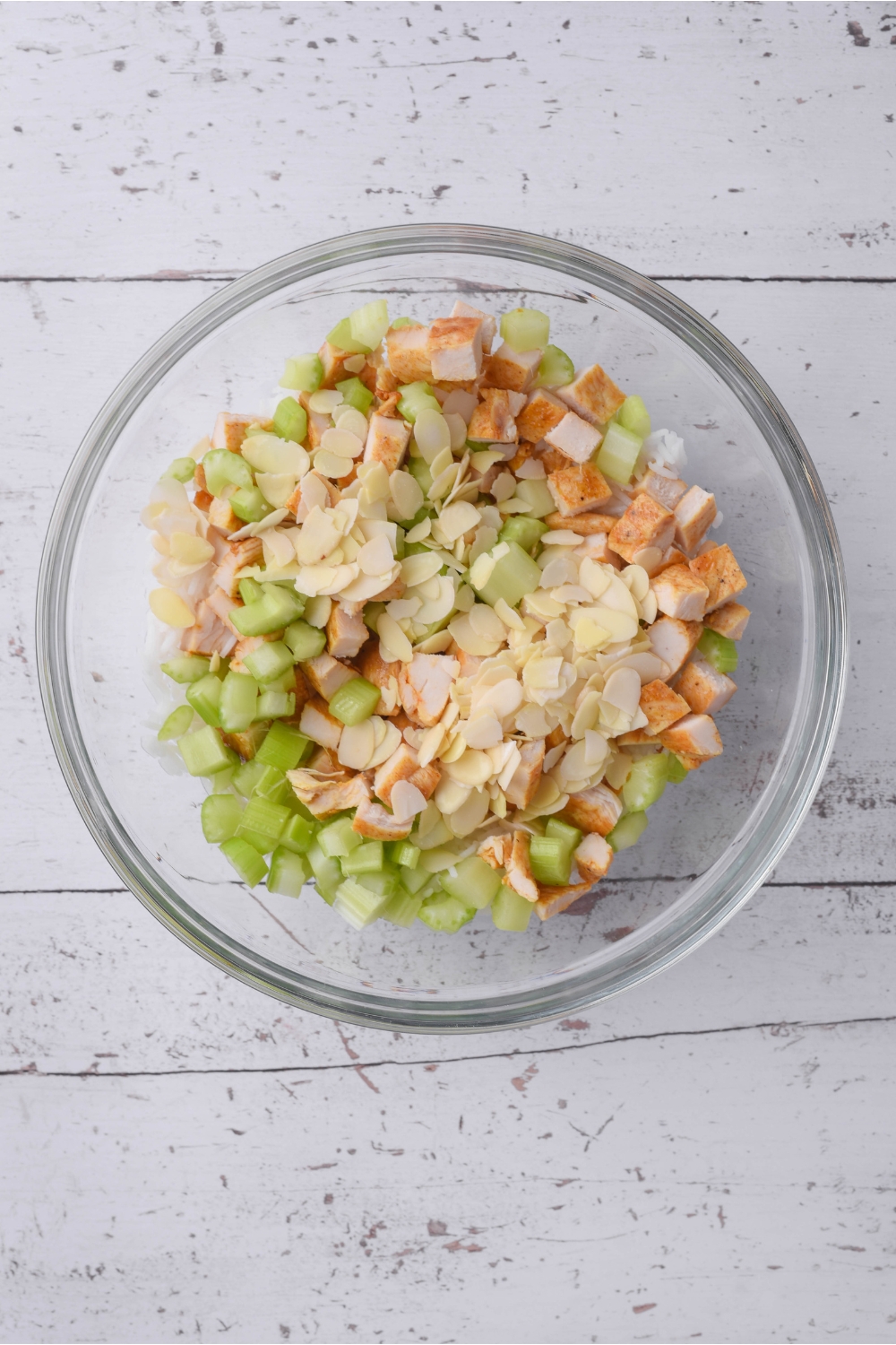 A clear bowl filled with chopped celery, slivered almonds, chopped chicken, and white rice.