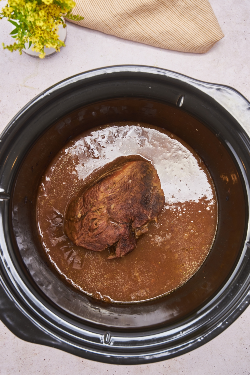 A crockpot filled with cooked and browned eye of round roast in a seasoned liquid.