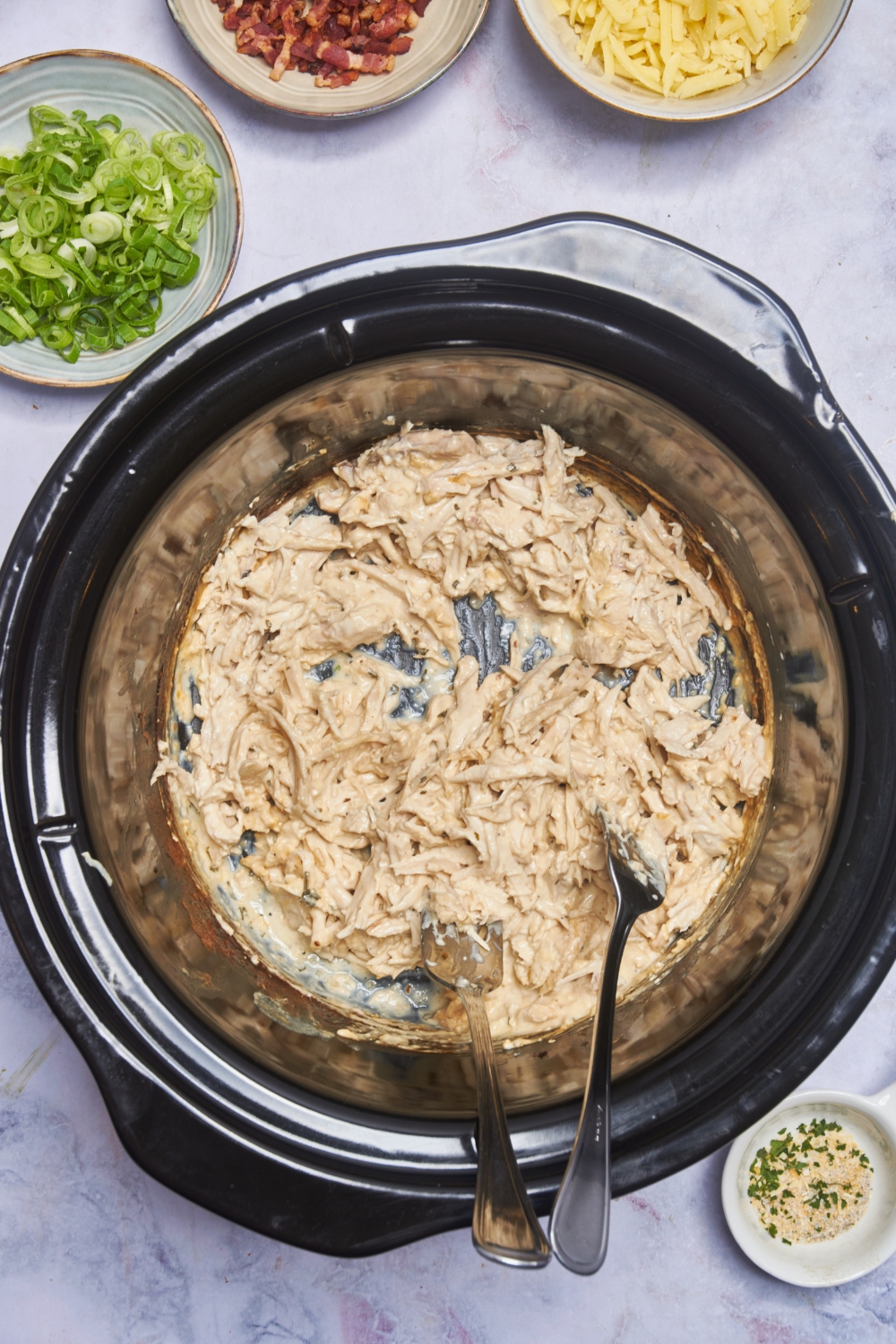A crock pot filled with cooked and shredded chicken in a creamy seasoned sauce.