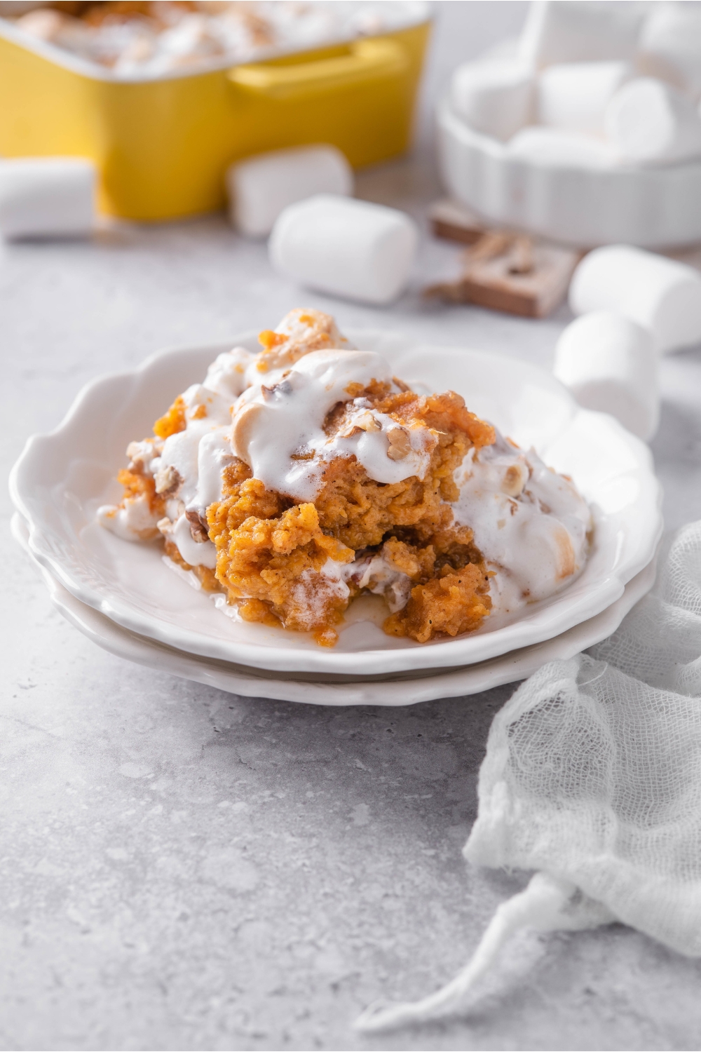 A serving of sweet potato casserole on two white plates with marshmallows melting on top of the casserole.