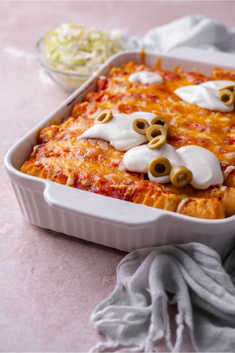 Taco tater tot casserole in a white casserole dish topped with golden brown melted cheese, sour cream, and sliced green olives.