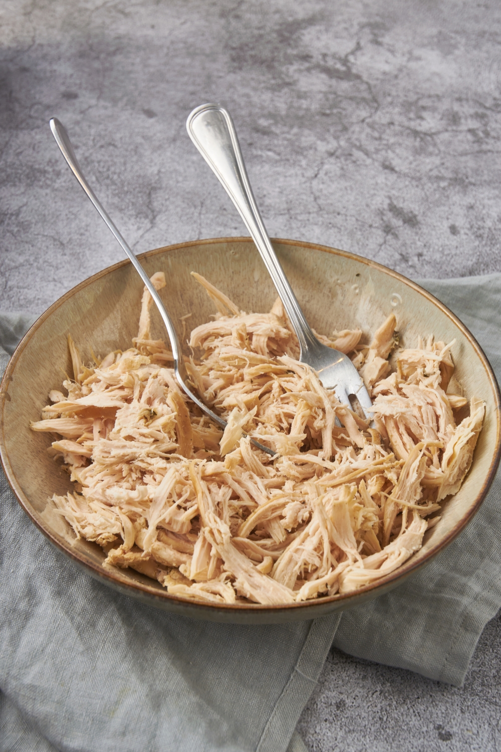 A bowl of shredded chicken with two forks in the bowl.