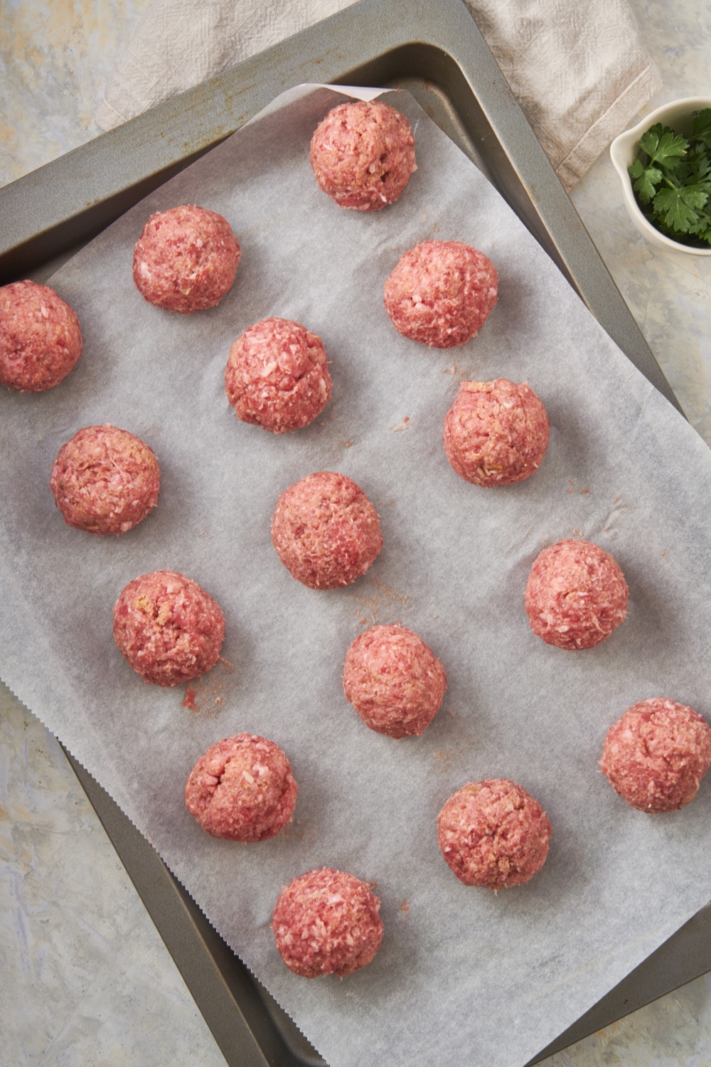 Fifteen unbaked meatballs spread evenly on a baking sheet lined with parchment paper.