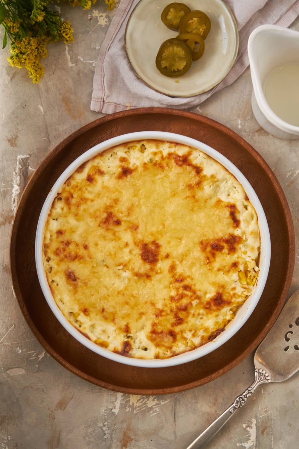 Overhead view of a white round baking dish filled with baked cream cheese corn casserole. The casserole is on top of a wooden plate.