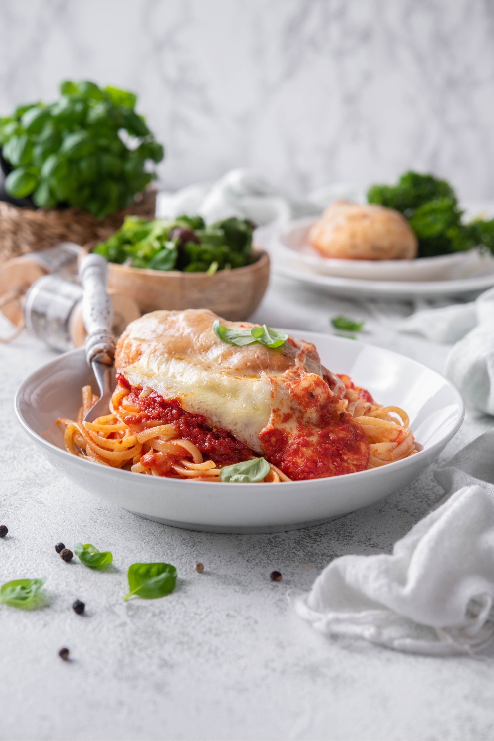 A bowl of chicken parmesan with chicken covered in melted cheese, a garnish of fresh basil, and served on a bed of pasta with marinara sauce.