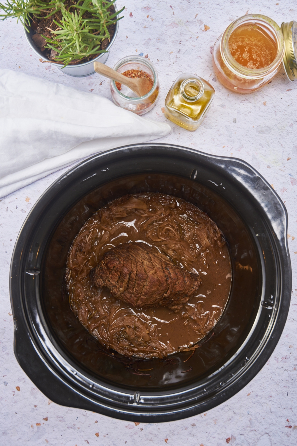 A black crockpot filled with cooked steak, a brown gravy, and cooked onions.