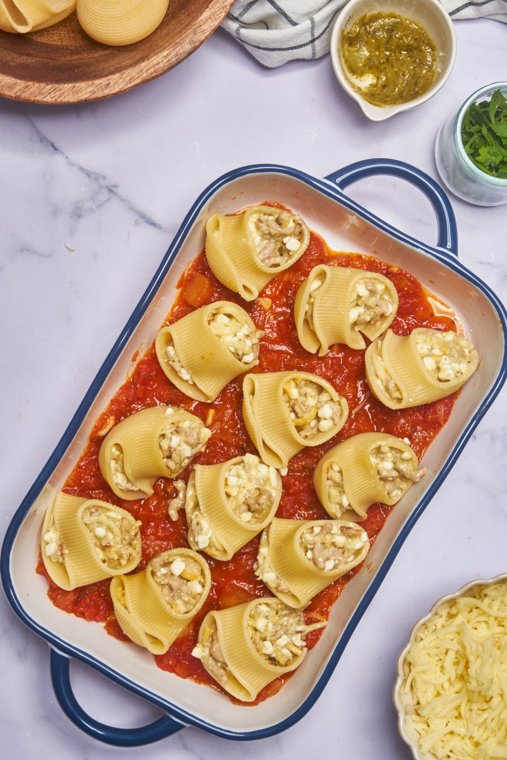 A blue-handled baking dish layered with red sauce and twelve pasta shells stuffed with a cheese and ground meat mixture.