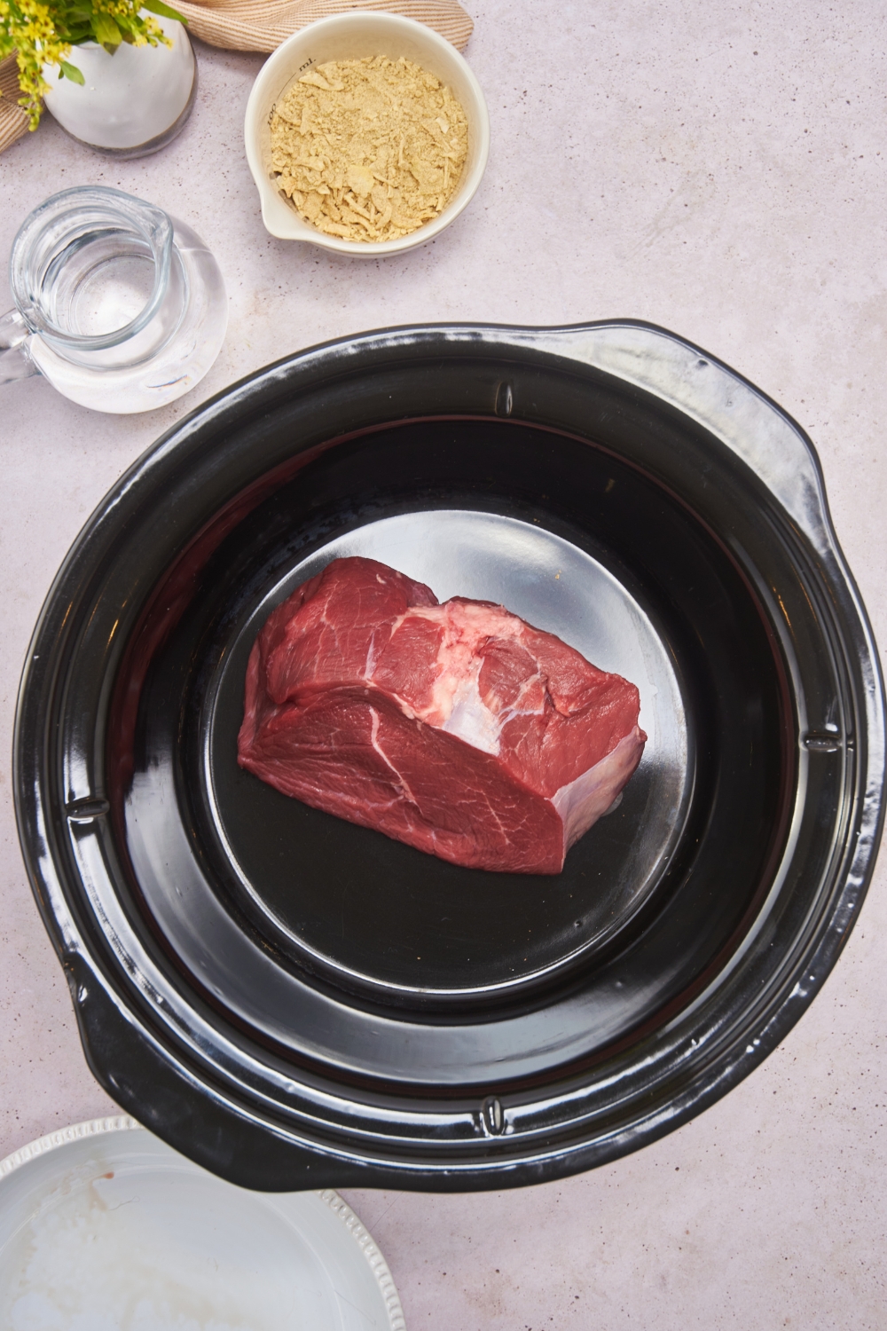 A crockpot with a raw beef roast in the bottom.