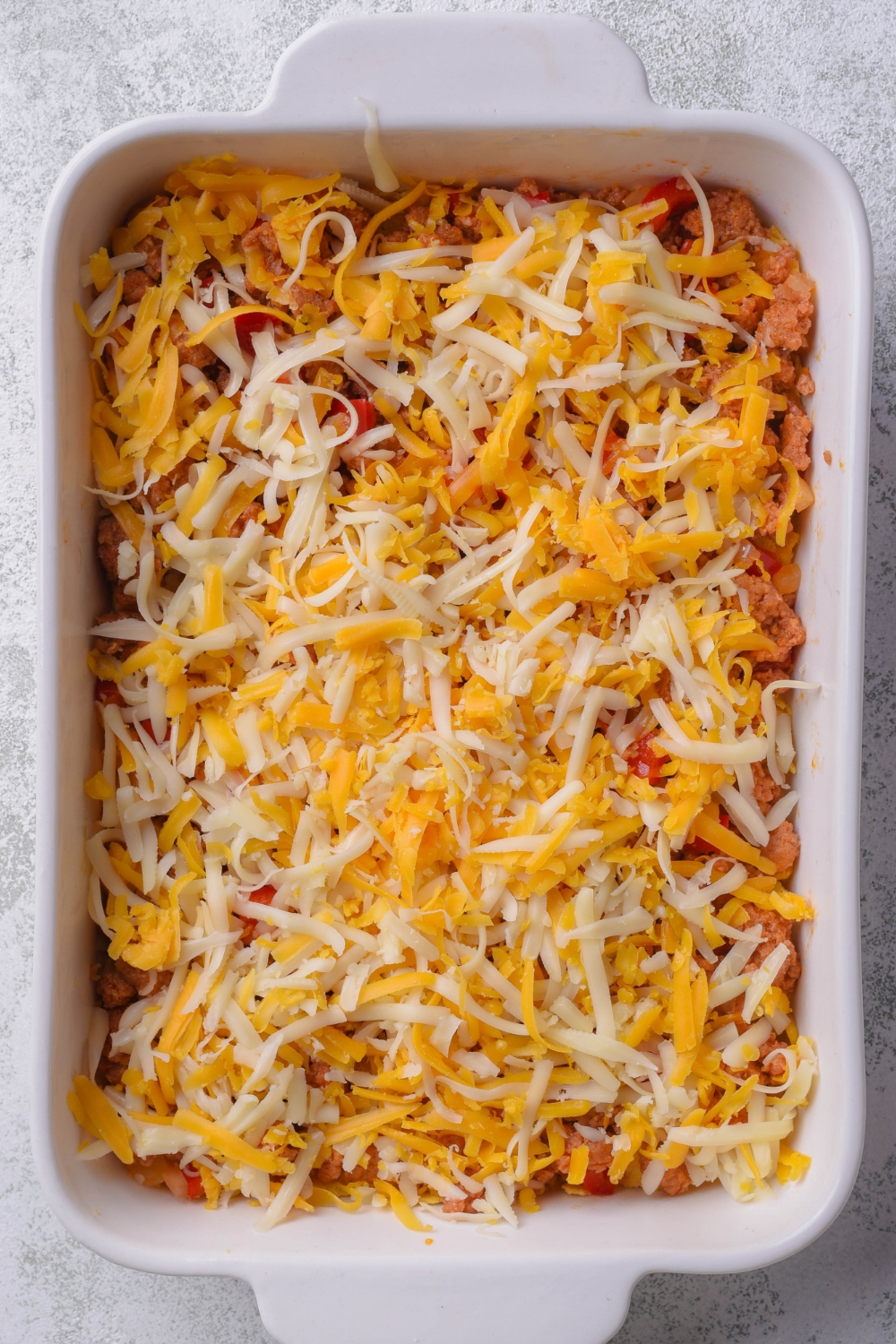 A casserole baking dish with a layer of tortilla chips and cooked chorizo, onions and peppers and a layer of shredded cheese.