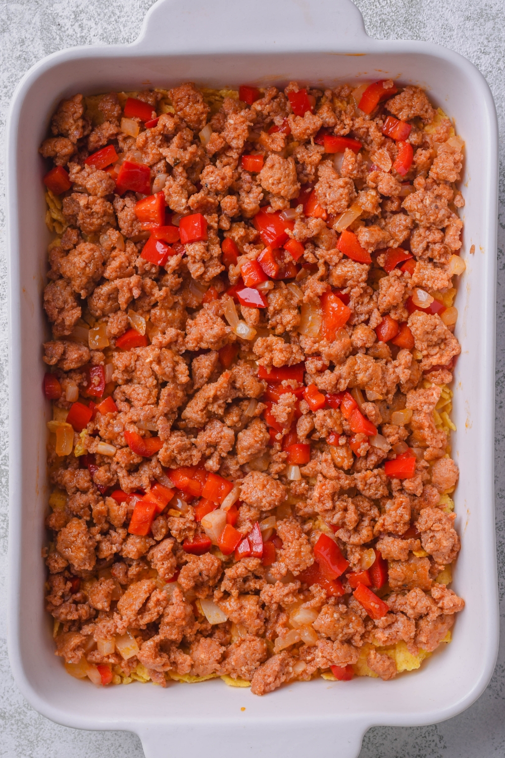 A casserole baking dish with a layer of tortilla chips and cooked chorizo, onions and peppers in it.