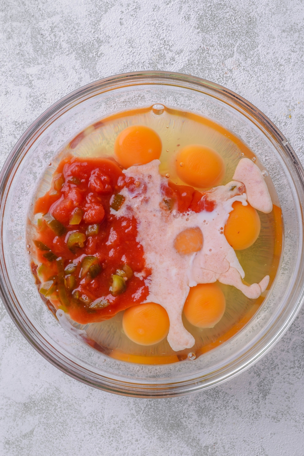 A bowl with egg, milk, and diced tomatoes.