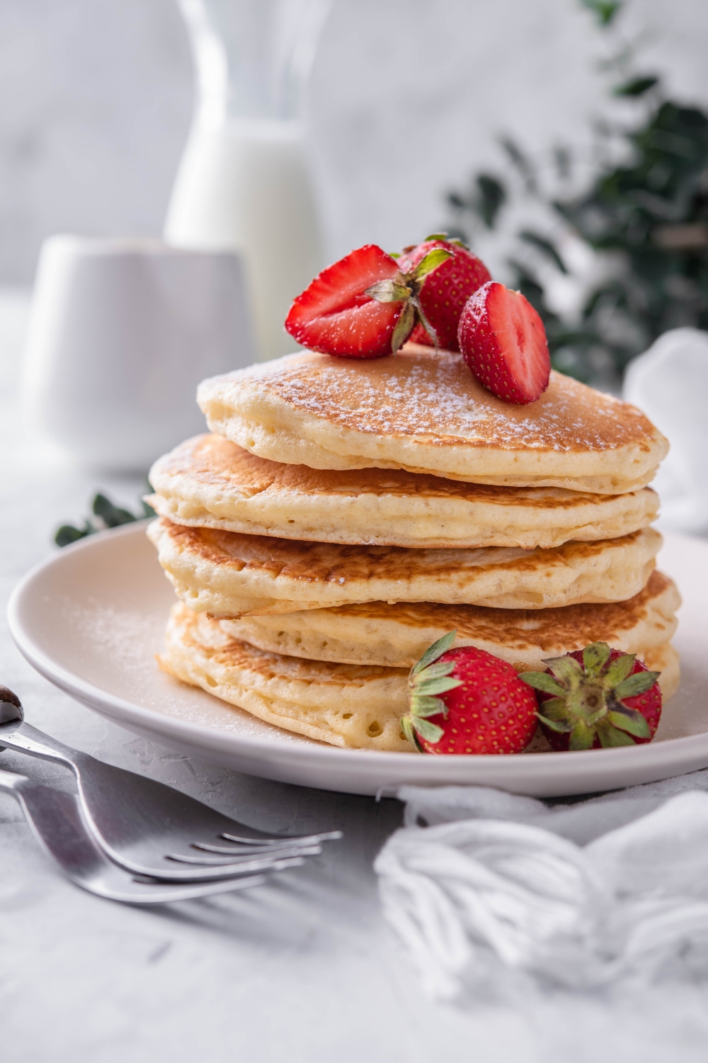A stack of pancakes on a plate with sliced strawberries sprinkled with powdered sugar.