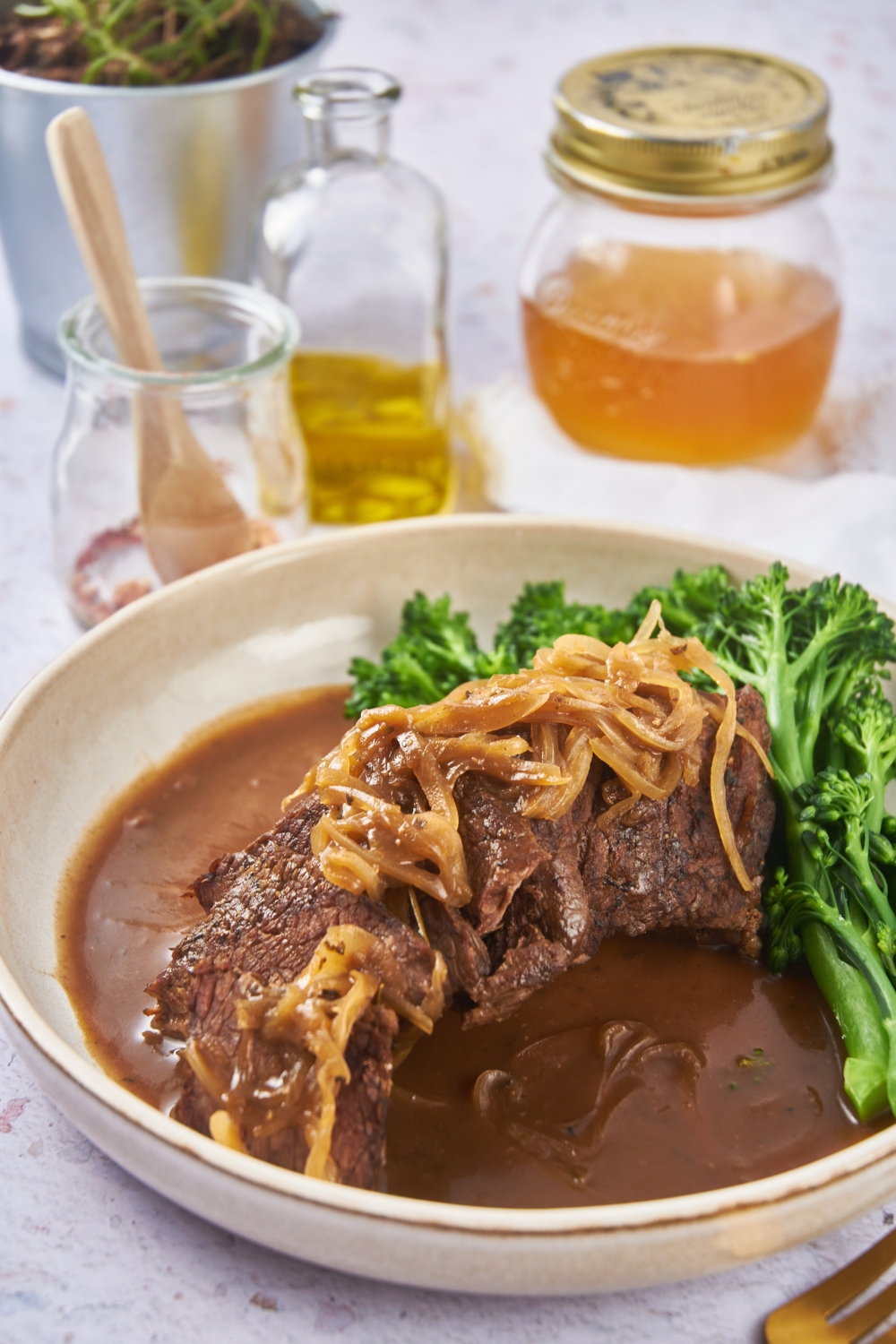 Sirloin roast topped with caramelized onions and covered in a brown gravy, with a side of broccoli.