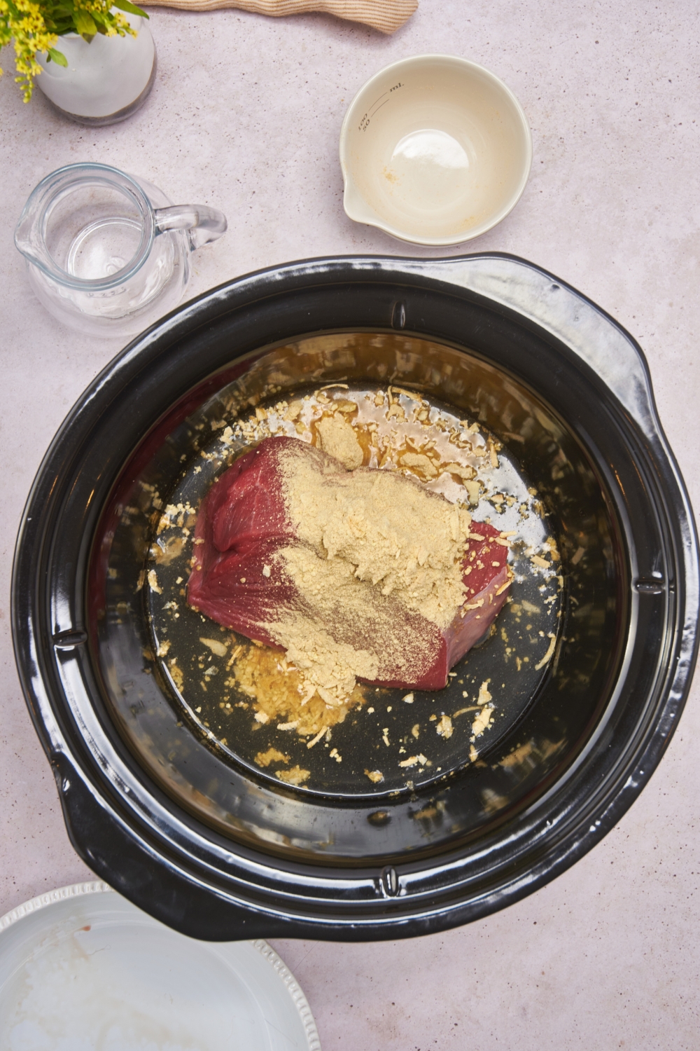A crockpot filled with raw eye of round beef roast covered in dry onion soup mix.