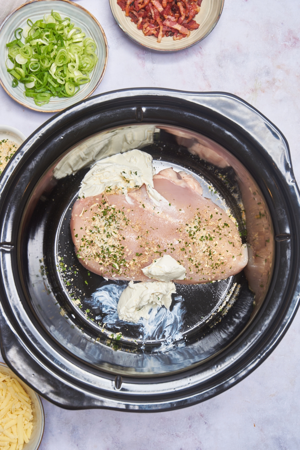 A crock pot with a raw chicken breast, ranch seasoning mix, and cream cheese in it.