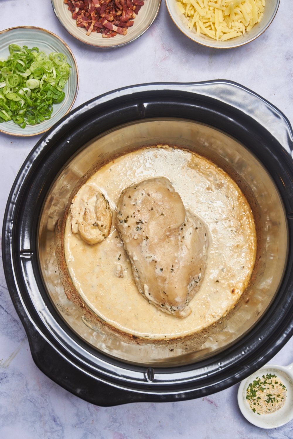 A cooked and seasoned chicken breast in a crock pot with a creamy seasoned sauce.