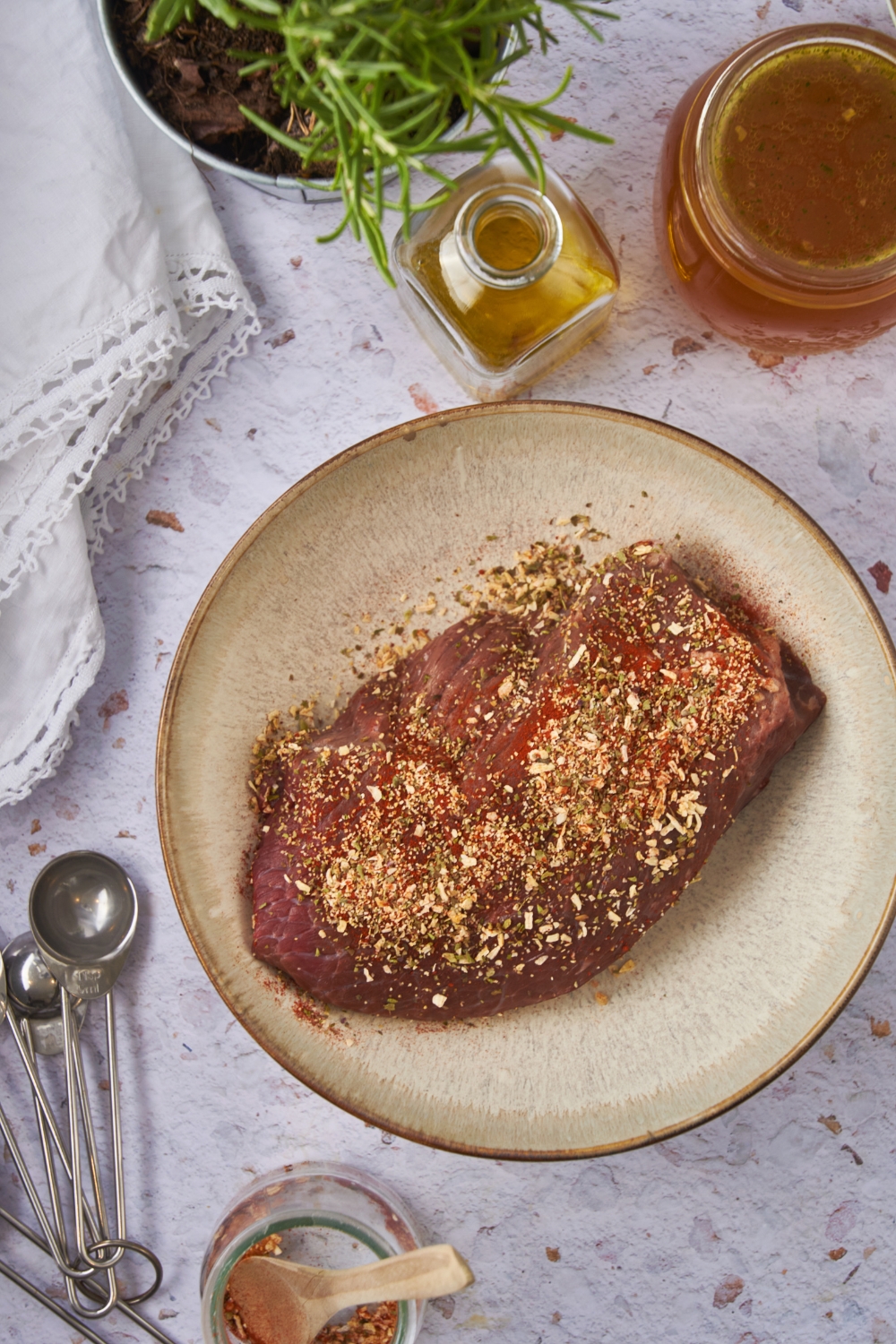 A seasoned sirloin steak in a shallow bowl surrounded by an assortment of ingredients.