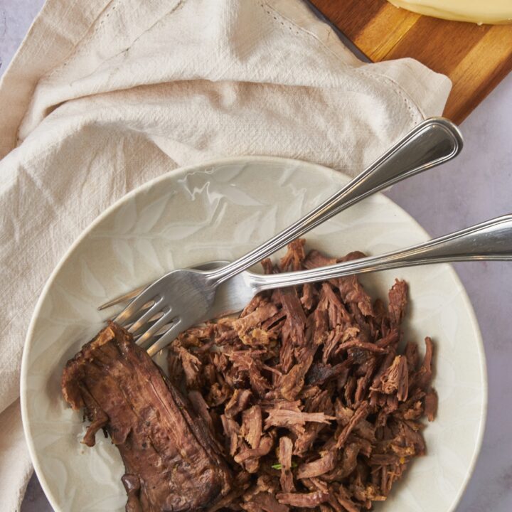 A bowl of cooked and shredded tri tip with two forks in the bowl.