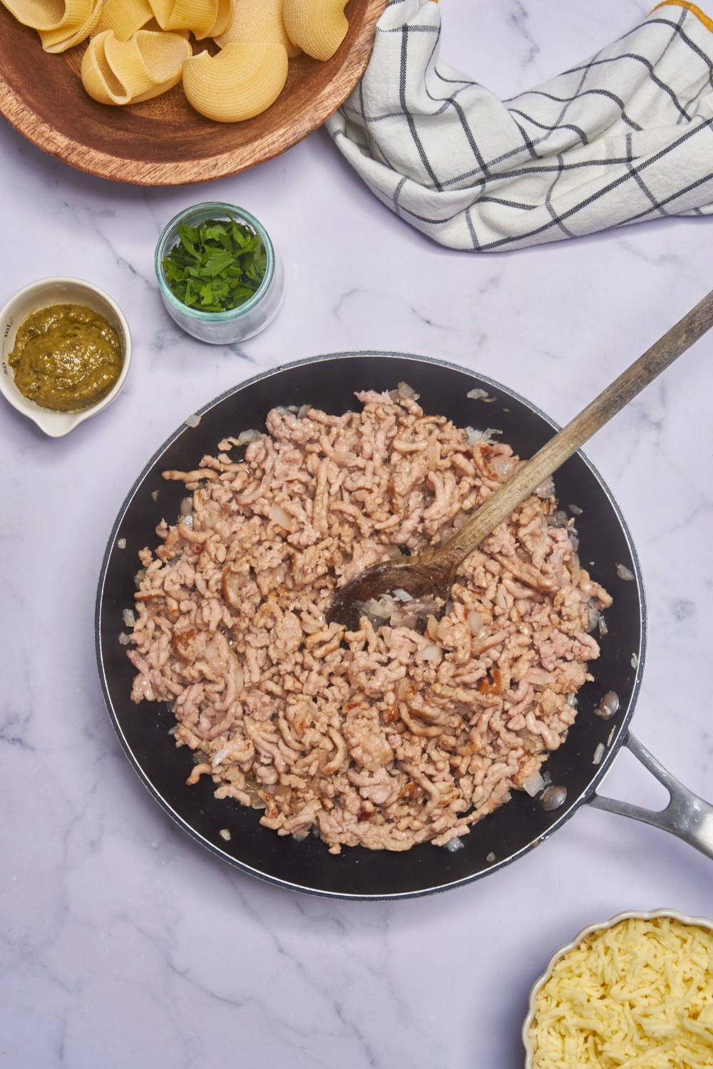 A black skillet filled with browned ground meat and diced onions being stirred with a wooden spoon.